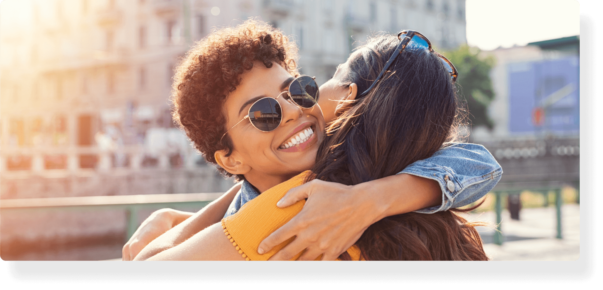 Two women hug in a parking lot as one comes to visit