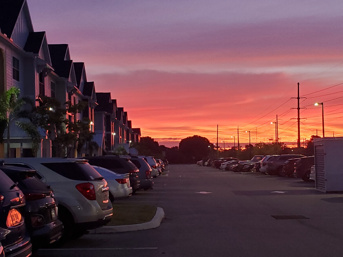 A row of multifamily apartments with cars parked out front and the sun setting over Florida in the background