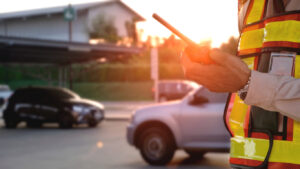 Resident with a service job in a safety vest using phone in outdoor parking lot area where they spark their vehicle on private apartment property